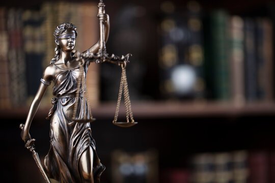 Escultura da Justiça com uma balança, em frente a uma biblioteca jurídica